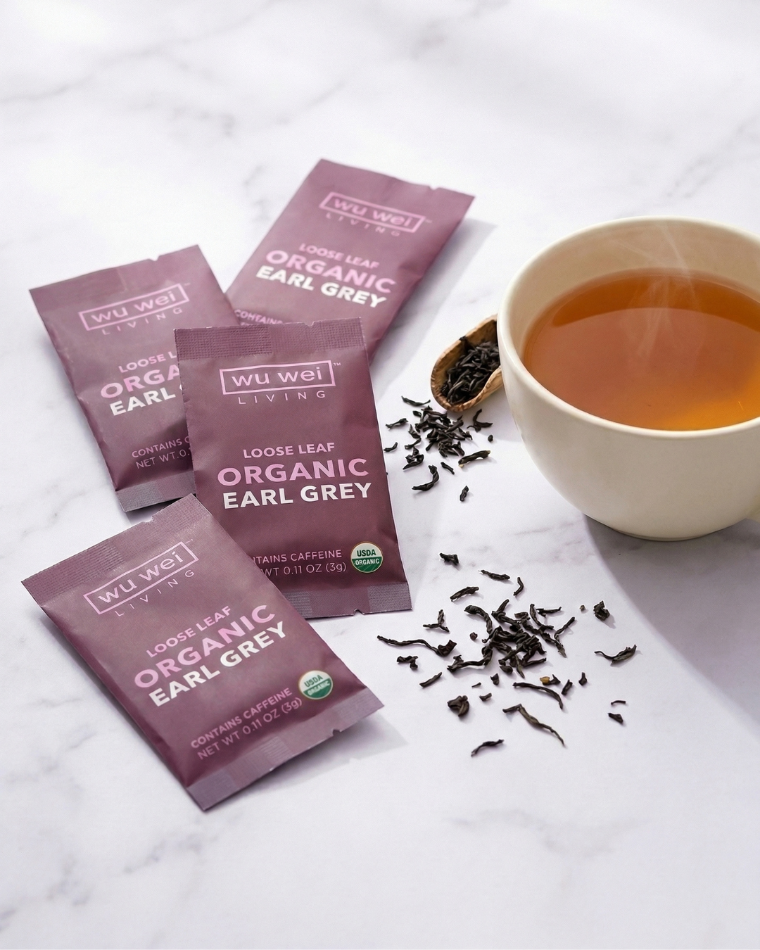 Wu Wei Living Organic Earl Grey tea packages with a cup of tea on a white marble surface — Wu Wei Living