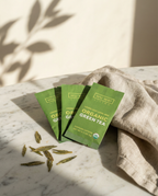 Organic Green Tea Wu Wei Living. Green tea packages on a marble surface with a beige cloth and tea leaves.