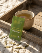 Wu Wei Living organic green tea package with a steaming cup of tea on a wooden tray.