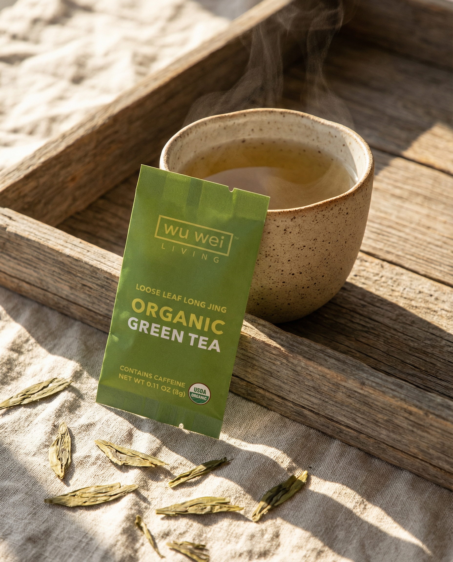 Wu Wei Living organic green tea package with a steaming cup of tea on a wooden tray.