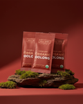 Three packages of Wu Wei Living Organic Oolong tea on a red background with greenery.