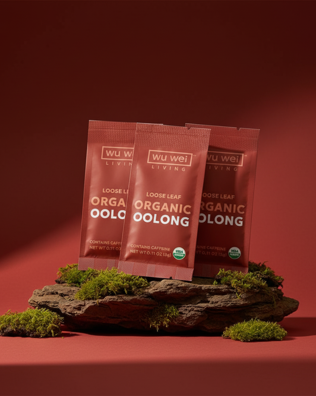 Three packages of Wu Wei Living Organic Oolong tea on a red background with greenery.