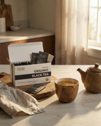 Box of Wu Wei Living Organic Black Tea with a cup and teapot on a kitchen counter