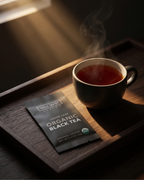 Steaming cup of tea on a wooden tray with a Wu Wei Living Loose Leaf Organic Black Tea package.
