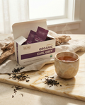 Box of Wu Wei Organic Earl Grey tea with tea leaves and a cup on a marble surface.