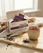 Box of Wu Wei Organic Earl Grey tea with tea leaves and a cup on a marble surface.