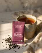 Wu Wei Living Organic Earl Grey tea package with a steaming cup of tea on a marble surface.