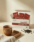 Box of Wu Wei Organic Oolong Tea with tea leaves and a cup on a light background