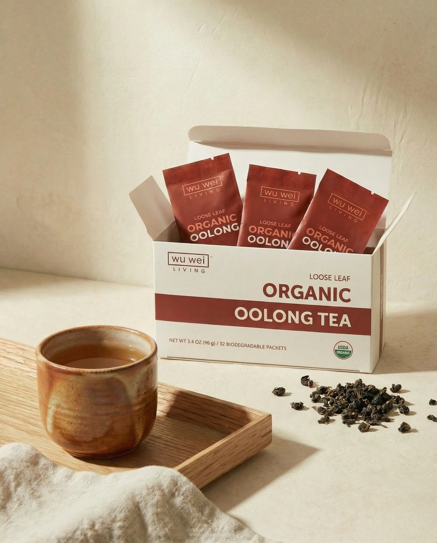 Box of Wu Wei Organic Oolong Tea with tea leaves and a cup on a light background