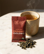 Wu Wei Living Organic Oolong tea package with a cup of tea and loose leaves on a marble surface.