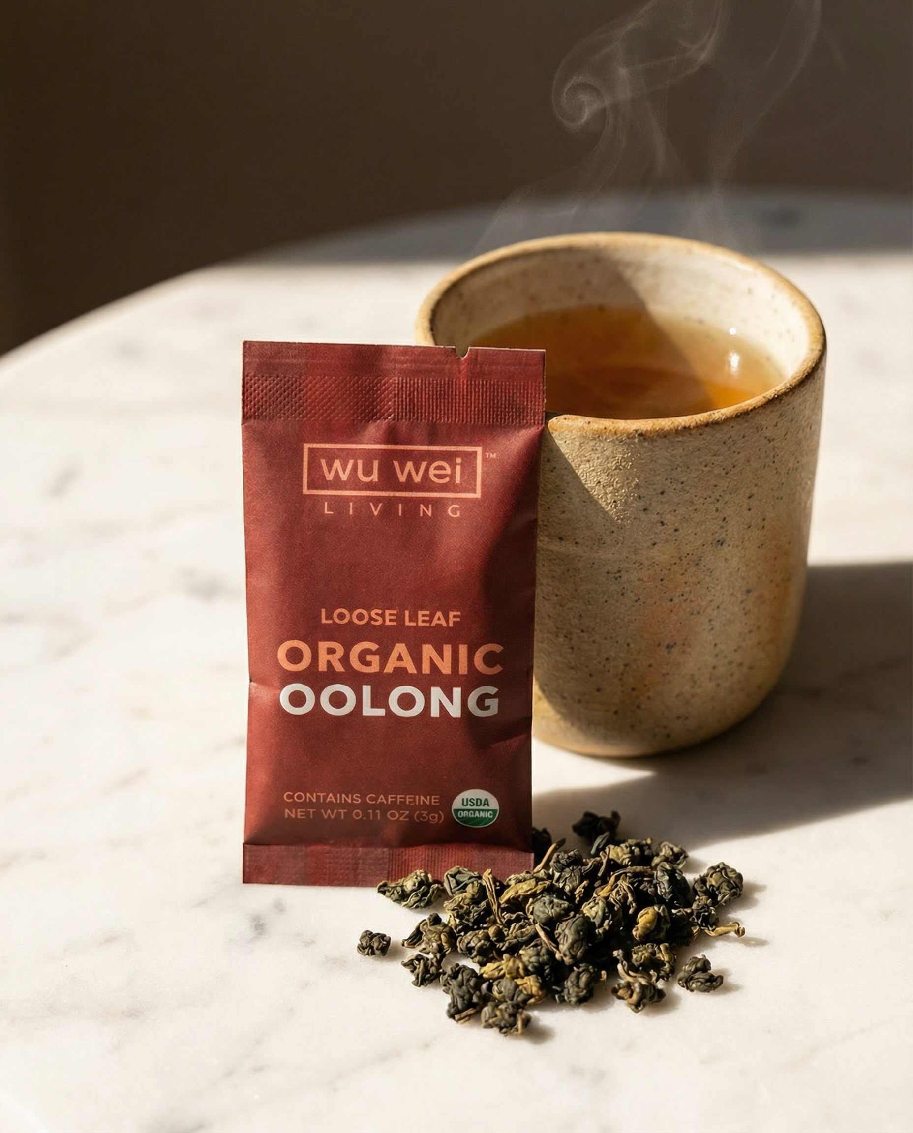 Wu Wei Living Organic Oolong tea package with a cup of tea and loose leaves on a marble surface.
