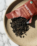 Loose leaf tea spilling out of a red package - Wu Wei Living Organic Oolong