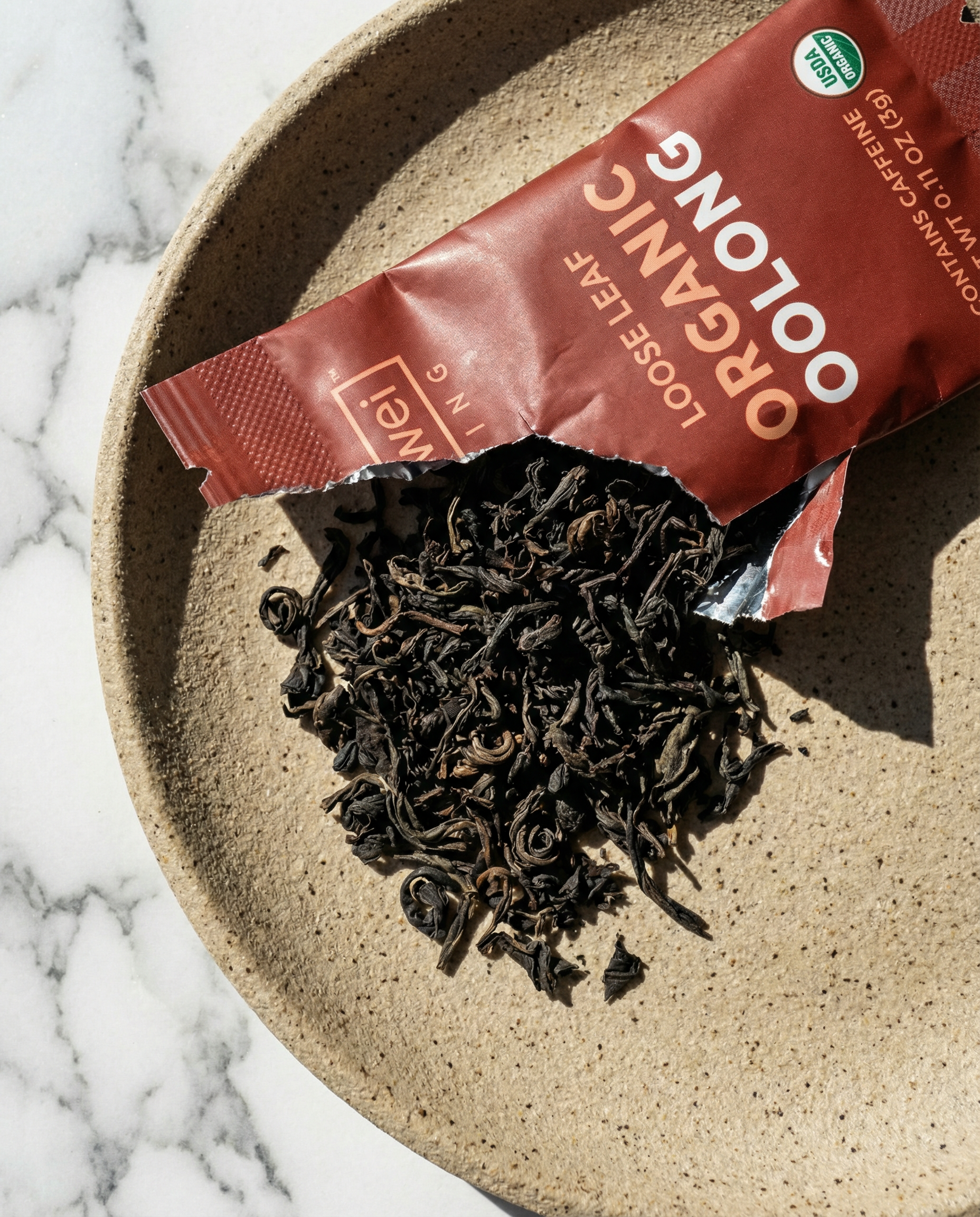 Loose leaf tea spilling out of a red package - Wu Wei Living Organic Oolong