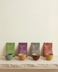 Four Wu Wei Living tea bags with corresponding cups on a wooden surface against a beige background