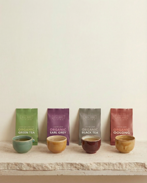 Four Wu Wei Living tea bags with corresponding cups on a wooden surface against a beige background
